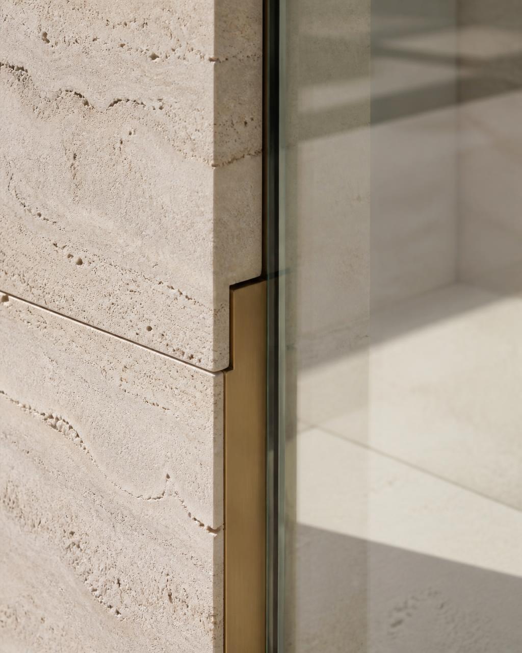 Close detail of travertine, plaster and brushed brass meeting in raking light